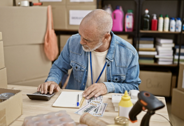 A man works on bills in backroom with boxes.